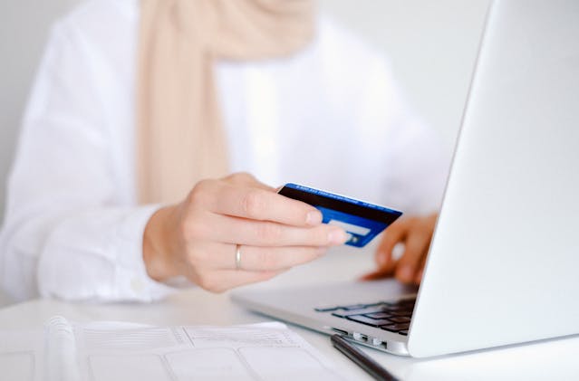 a person holding a credit card in front of a laptop